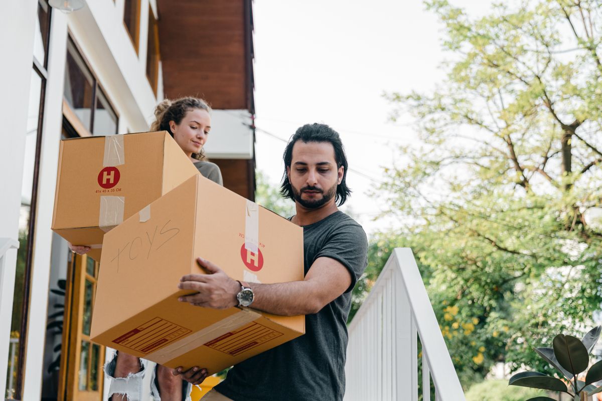 Two people carrying moving boxes outside a home