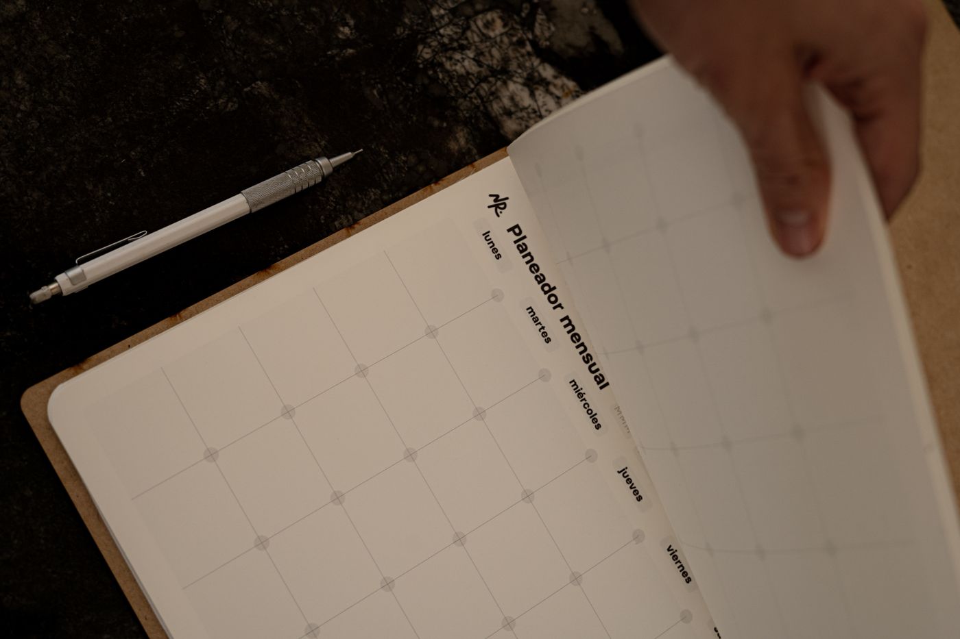 Hand turning a page of an undated monthly planner.
