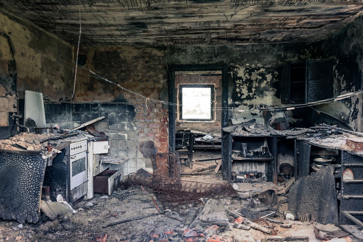 Damaged kitchen interior with debris and blackened surfaces